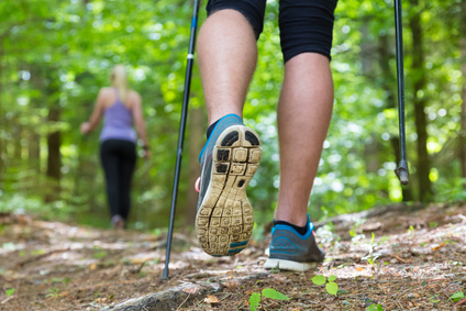 Young fit couple hiking in nature. Adventure, sport and exercise. Detail of male step, legs and nordic walking poles in green woods.
